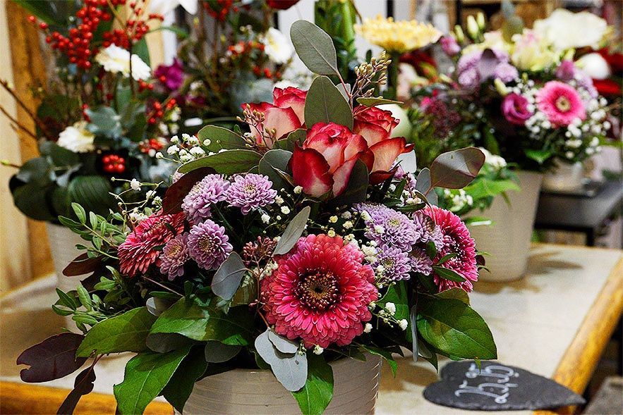 Ein florales Arrangement mit bunten Blumen und grünen Blättern in einem dekorativen Topf.
